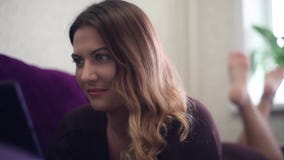 Κινηματογράφηση σε πρώτο πλάνο Το όμορφο νέο κορίτσι απολαμβάνει μια ταμπλέτα στον καναπέ Εγχώριο ύφος απόθεμα βίντεο Κινηματογράφηση σε πρώτο πλάνο Το όμορφο νέο κορίτσι απολαμβάνει μια ταμπλέτα στον καναπέ Εγχώριο ύφος απόθεμα βίντεο