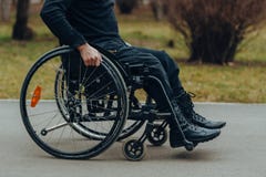 Κινηματογράφηση σε πρώτο πλάνο του αρσενικού χεριού στη ρόδα της αναπηρικής καρέκλας κατά τη διάρκεια του περιπάτου στο πάρκο στοκ εικόνα Κινηματογράφηση σε πρώτο πλάνο του αρσενικού χεριού στη ρόδα της αναπηρικής καρέκλας κατά τη διάρκεια του περιπάτου στο πάρκο στοκ εικόνα