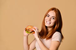 Κλείστε επάνω το πορτρέτο μιας πεινασμένης νέας γυναίκας που τρώει burger πέρα από το nude υπόβαθρο στοκ εικόνα Κλείστε επάνω το πορτρέτο μιας πεινασμένης νέας γυναίκας που τρώει burger πέρα από το nude υπόβαθρο στοκ εικόνα