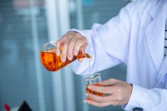 Κλείστε επάνω το χέρι επιστημόνων που χύνει το πορτοκαλί υγρό στοκ φωτογραφία Κλείστε επάνω το χέρι επιστημόνων που χύνει το πορτοκαλί υγρό στοκ φωτογραφία