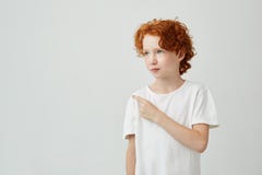 Κλείστε επάνω του αρκετά σγουρού redhead αγοριού με τις φακίδες στην άσπρη μπλούζα που εξετάζει κατά μέρος, που δείχνει τον άσπρο στοκ φωτογραφία με δικαίωμα ελεύθερης χρήσης Κλείστε επάνω του αρκετά σγουρού redhead αγοριού με τις φακίδες στην άσπρη μπλούζα που εξετάζει κατά μέρος, που δείχνει τον άσπρο στοκ φωτογραφία με δικαίωμα ελεύθερης χρήσης
