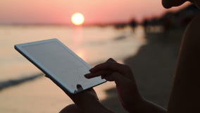 Κορίτσι που εργάζεται με το PC ταμπλετών στην παραλία στο ηλιοβασίλεμα Κορίτσι που εργάζεται με το PC ταμπλετών στην παραλία στο ηλιοβασίλεμα