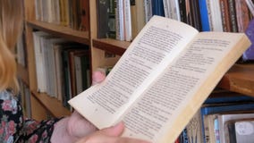Κορίτσι που κρατά το βιβλίο στα χέρια και που διαβάζει στη βιβλιοθήκη στο υπόβαθρο των ραφιών απόθεμα βίντεο Κορίτσι που κρατά το βιβλίο στα χέρια και που διαβάζει στη βιβλιοθήκη στο υπόβαθρο των ραφιών απόθεμα βίντεο