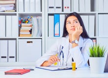 Κουρασμένος θηλυκός ιατρός στην άσπρη ιατρική εσθήτα επιδέσμου που περιμένει τους ασθενείς στο γραφείο Στοκ φωτογραφία με δικαίωμα ελεύθερης χρήσης Κουρασμένος θηλυκός ιατρός στην άσπρη ιατρική εσθήτα επιδέσμου που περιμένει τους ασθενείς στο γραφείο Στοκ φωτογραφία με δικαίωμα ελεύθερης χρήσης