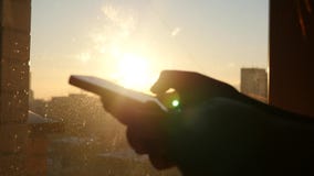 Κρατήστε το τηλέφωνο στο χέρι του σε ένα υπόβαθρο του ηλιοβασιλέματος, με το έντονο φως από τον ήλιο, σε αργή κίνηση φιλμ μικρού μήκους Κρατήστε το τηλέφωνο στο χέρι του σε ένα υπόβαθρο του ηλιοβασιλέματος, με το έντονο φως από τον ήλιο, σε αργή κίνηση φιλμ μικρού μήκους