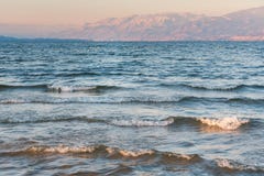 Κύματα που συντρίβουν επάνω στην παραλία στο ηλιοβασίλεμα με τα χιονισμένα βουνά στο υπόβαθρο Στοκ Εικόνα Κύματα που συντρίβουν επάνω στην παραλία στο ηλιοβασίλεμα με τα χιονισμένα βουνά στο υπόβαθρο Στοκ Εικόνα