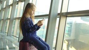 Λατρευτό μικρό κορίτσι στον αερολιμένα κοντά στο μεγάλο παιχνίδι παραθύρων με το τηλέφωνό της απόθεμα βίντεο Λατρευτό μικρό κορίτσι στον αερολιμένα κοντά στο μεγάλο παιχνίδι παραθύρων με το τηλέφωνό της απόθεμα βίντεο