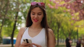 Μήνυμα ανάγνωσης γυναικών στο smartphone που περπατά στο θερινό πάρκο φιλμ μικρού μήκους Μήνυμα ανάγνωσης γυναικών στο smartphone που περπατά στο θερινό πάρκο φιλμ μικρού μήκους