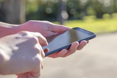 Μαύρο smartphone υπό εξέταση στο πάρκο υπαίθρια, αναμμένο από τον ήλιο στοκ φωτογραφίες με δικαίωμα ελεύθερης χρήσης Μαύρο smartphone υπό εξέταση στο πάρκο υπαίθρια, αναμμένο από τον ήλιο στοκ φωτογραφίες με δικαίωμα ελεύθερης χρήσης