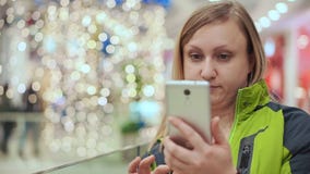 Μια γυναίκα εξετάζει ένα smartphone στην έκπληξη, στέκεται σε ένα εμπορικό κέντρο, σε ένα κλίμα μιας λάμπας φωτός φιλμ μικρού μήκους Μια γυναίκα εξετάζει ένα smartphone στην έκπληξη, στέκεται σε ένα εμπορικό κέντρο, σε ένα κλίμα μιας λάμπας φωτός φιλμ μικρού μήκους