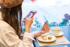 Μια γυναίκα με ένα smartphone παίρνει μια εικόνα macaroons και ένα φλυτζάνι του τσαγιού σε έναν καφέ στοκ φωτογραφία Μια γυναίκα με ένα smartphone παίρνει μια εικόνα macaroons και ένα φλυτζάνι του τσαγιού σε έναν καφέ στοκ φωτογραφία