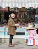 Μια ηλικιωμένη γυναίκα διαβάζει μια εφημερίδα έξω από ένα κατάστημα εφημερίδων Στο μετρητή είναι περιοδικά και εφημερίδες στοκ φωτογραφία με δικαίωμα ελεύθερης χρήσης Μια ηλικιωμένη γυναίκα διαβάζει μια εφημερίδα έξω από ένα κατάστημα εφημερίδων Στο μετρητή είναι περιοδικά και εφημερίδες στοκ φωτογραφία με δικαίωμα ελεύθερης χρήσης
