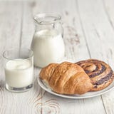 Μια κανάτα του γάλακτος και ορεκτικός ένας croissant σε έναν του χωριού πίνακα το πρωί ligh στοκ φωτογραφία Μια κανάτα του γάλακτος και ορεκτικός ένας croissant σε έναν του χωριού πίνακα το πρωί ligh στοκ φωτογραφία