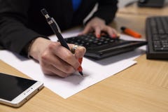 Μια κινηματογράφηση σε πρώτο πλάνο, επιχειρησιακή κυρία, που γράφει σε ένα κομμάτι χαρτί, κάθεται στο γραφείο της στοκ εικόνες Μια κινηματογράφηση σε πρώτο πλάνο, επιχειρησιακή κυρία, που γράφει σε ένα κομμάτι χαρτί, κάθεται στο γραφείο της στοκ εικόνες