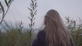 Μια νέα γυναίκα περπατά ενάντια στο σκηνικό της λίμνης μεταξύ της πολύ υψηλής πράσινης χλόης φιλμ μικρού μήκους Μια νέα γυναίκα περπατά ενάντια στο σκηνικό της λίμνης μεταξύ της πολύ υψηλής πράσινης χλόης φιλμ μικρού μήκους