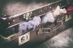 Μια παλαιά καφετιά βαλίτσα, κοντά, προεξέχοντα ενδύματα και πόδια μιας κούκλας στοκ εικόνα Μια παλαιά καφετιά βαλίτσα, κοντά, προεξέχοντα ενδύματα και πόδια μιας κούκλας στοκ εικόνα