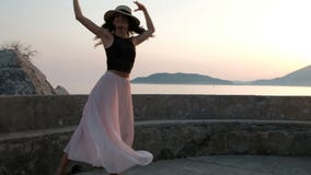 Μια όμορφη γυναίκα στα υψηλά τακούνια και σε ένα ελαφρύ φόρεμα χορεύει χαριτωμένα με ένα καπέλο στην πλατφόρμα απόθεμα βίντεο Μια όμορφη γυναίκα στα υψηλά τακούνια και σε ένα ελαφρύ φόρεμα χορεύει χαριτωμένα με ένα καπέλο στην πλατφόρμα απόθεμα βίντεο
