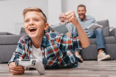 Μικρό παιδί που εναπόκειται στο gamepad στο πάτωμα ενθαρρυντικό, ενώ ο πατέρας και ο παππούς του είναι στοκ φωτογραφία Μικρό παιδί που εναπόκειται στο gamepad στο πάτωμα ενθαρρυντικό, ενώ ο πατέρας και ο παππούς του είναι στοκ φωτογραφία