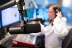 Μικρόφωνο στούντιο στο ραδιοσταθμό με το θηλυκό οικοδεσπότη στο υπόβαθρο στοκ εικόνα με δικαίωμα ελεύθερης χρήσης Μικρόφωνο στούντιο στο ραδιοσταθμό με το θηλυκό οικοδεσπότη στο υπόβαθρο στοκ εικόνα με δικαίωμα ελεύθερης χρήσης