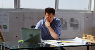 Μπροστινή άποψη του ασιατικού αρσενικού αρχιτέκτονα που χρησιμοποιεί το lap-top στο γραφείο σε ένα σύγχρονο γραφείο 4k φιλμ μικρού μήκους Μπροστινή άποψη του ασιατικού αρσενικού αρχιτέκτονα που χρησιμοποιεί το lap-top στο γραφείο σε ένα σύγχρονο γραφείο 4k φιλμ μικρού μήκους