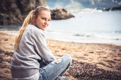Μόνη συνεδρίαση τουριστών γυναικών χαμόγελου στην παραλία στη συννεφιάζω ημέρα και εξέταση τη κάμερα στοκ εικόνες Μόνη συνεδρίαση τουριστών γυναικών χαμόγελου στην παραλία στη συννεφιάζω ημέρα και εξέταση τη κάμερα στοκ εικόνες