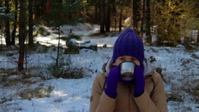 Νέα γυναίκα που πίνει το καυτό τσάι ή τον καφέ στο χειμερινό δάσος απόθεμα βίντεο Νέα γυναίκα που πίνει το καυτό τσάι ή τον καφέ στο χειμερινό δάσος απόθεμα βίντεο