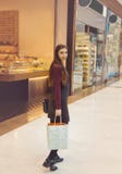 Νέα γυναίκα που χαμογελά και που κρατά τις τσάντες αγορών περπατώντας στη λεωφόρο αγορών στοκ εικόνα με δικαίωμα ελεύθερης χρήσης Νέα γυναίκα που χαμογελά και που κρατά τις τσάντες αγορών περπατώντας στη λεωφόρο αγορών στοκ εικόνα με δικαίωμα ελεύθερης χρήσης