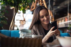 Νέα γυναίκα που χαμογελά με το smartphone διαθέσιμο στο εστιατόριο με το θολωμένο υπόβαθρο στοκ εικόνα Νέα γυναίκα που χαμογελά με το smartphone διαθέσιμο στο εστιατόριο με το θολωμένο υπόβαθρο στοκ εικόνα