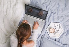 Νέα γυναίκα στο άσπρο πουλόβερ που βρίσκεται στο κρεβάτι και που χρησιμοποιεί το lap-top στοκ εικόνες Νέα γυναίκα στο άσπρο πουλόβερ που βρίσκεται στο κρεβάτι και που χρησιμοποιεί το lap-top στοκ εικόνες