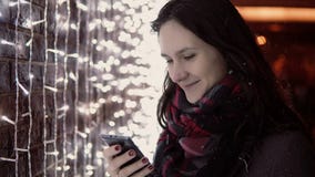 Νέα ελκυστική γυναίκα που χρησιμοποιεί το smartphone στο μειωμένο χιόνι στη νύχτα Χριστουγέννων που στέκεται κοντά στον τοίχο φω' φιλμ μικρού μήκους Νέα ελκυστική γυναίκα που χρησιμοποιεί το smartphone στο μειωμένο χιόνι στη νύχτα Χριστουγέννων που στέκεται κοντά στον τοίχο φω' φιλμ μικρού μήκους