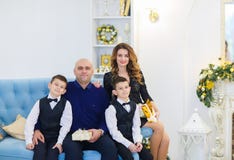Νέα ευτυχής συνεδρίαση μητέρων και πατέρων στον καναπέ με τους γιους στο διακοσμημένο δωμάτιο για τις διακοπές Χριστουγέννων στοκ φωτογραφίες με δικαίωμα ελεύθερης χρήσης Νέα ευτυχής συνεδρίαση μητέρων και πατέρων στον καναπέ με τους γιους στο διακοσμημένο δωμάτιο για τις διακοπές Χριστουγέννων στοκ φωτογραφίες με δικαίωμα ελεύθερης χρήσης