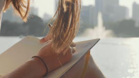 Νέα συνεδρίαση γυναικών στον πάγκο στο πάρκο και το γράψιμο στο ημερολόγιο, κινηματογράφηση σε πρώτο πλάνο απόθεμα βίντεο Νέα συνεδρίαση γυναικών στον πάγκο στο πάρκο και το γράψιμο στο ημερολόγιο, κινηματογράφηση σε πρώτο πλάνο απόθεμα βίντεο
