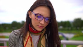 Νέα όμορφη γυναίκα με eyeglasses που διαβάζει μια συνεδρίαση βιβλίων σε έναν πάγκο έξω σε ένα πάρκο το καλοκαίρι Κλείστε επάνω το απόθεμα βίντεο Νέα όμορφη γυναίκα με eyeglasses που διαβάζει μια συνεδρίαση βιβλίων σε έναν πάγκο έξω σε ένα πάρκο το καλοκαίρι Κλείστε επάνω το απόθεμα βίντεο