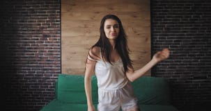 Νέο brunette γυναικών στις πυτζάμες μπροστά από τη κάμερα που πηδά και που χορεύει που διεγείρεται το πρωί στο σύγχρονο στούντιό απόθεμα βίντεο Νέο brunette γυναικών στις πυτζάμες μπροστά από τη κάμερα που πηδά και που χορεύει που διεγείρεται το πρωί στο σύγχρονο στούντιό απόθεμα βίντεο