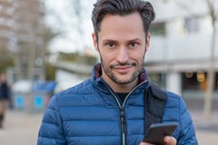 Νέο επιχειρησιακό χαμογελώντας άτομο στην οδό με ένα κινητό τηλέφωνο και μια μπλε ζακέτα στοκ εικόνα με δικαίωμα ελεύθερης χρήσης Νέο επιχειρησιακό χαμογελώντας άτομο στην οδό με ένα κινητό τηλέφωνο και μια μπλε ζακέτα στοκ εικόνα με δικαίωμα ελεύθερης χρήσης
