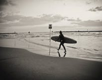 Νέο θηλυκό surfer με τον πίνακα που περπατά στην παραλία, που απεικονίζεται στο νερό, κάτω από έναν νεφελώδη ουρανό στοκ φωτογραφία Νέο θηλυκό surfer με τον πίνακα που περπατά στην παραλία, που απεικονίζεται στο νερό, κάτω από έναν νεφελώδη ουρανό στοκ φωτογραφία