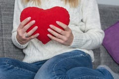 Νέο κορίτσι που κρατά το μεγάλο κόκκινο μαξιλάρι καρδιών διαθέσιμο στο στήθος της και που κάθεται στο κρεβάτι στοκ εικόνες με δικαίωμα ελεύθερης χρήσης Νέο κορίτσι που κρατά το μεγάλο κόκκινο μαξιλάρι καρδιών διαθέσιμο στο στήθος της και που κάθεται στο κρεβάτι στοκ εικόνες με δικαίωμα ελεύθερης χρήσης