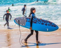 Νέο κορίτσι στα wetsuits με μια ιστιοσανίδα μια ηλιόλουστη ημέρα στην παραλία στοκ φωτογραφίες με δικαίωμα ελεύθερης χρήσης Νέο κορίτσι στα wetsuits με μια ιστιοσανίδα μια ηλιόλουστη ημέρα στην παραλία στοκ φωτογραφίες με δικαίωμα ελεύθερης χρήσης