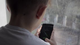 Νέο παίζοντας παιχνίδι αγοριών στο smartphone στο σπίτι Το αγόρι κάθεται στο windowsill μια βροχερή ημέρα Νέο παίζοντας παιχνίδι αγοριών στο smartphone στο σπίτι Το αγόρι κάθεται στο windowsill μια βροχερή ημέρα