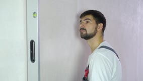 Νέος γενειοφόρος οικοδόμος που ελέγχει την ποιότητα του νέου τοίχου με το επίπεδο φυσαλίδων απόθεμα βίντεο Νέος γενειοφόρος οικοδόμος που ελέγχει την ποιότητα του νέου τοίχου με το επίπεδο φυσαλίδων απόθεμα βίντεο