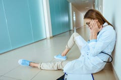 Νέος γιατρός σε μια συνεδρίαση παλτών εργαστηρίων σε ένα πάτωμα στο διάδρομο και το τρίψιμο νοσοκομείων στοκ φωτογραφία με δικαίωμα ελεύθερης χρήσης Νέος γιατρός σε μια συνεδρίαση παλτών εργαστηρίων σε ένα πάτωμα στο διάδρομο και το τρίψιμο νοσοκομείων στοκ φωτογραφία με δικαίωμα ελεύθερης χρήσης