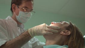 Νέος επιτυχής οδοντίατρος στη μάσκα που μεταχειρίζεται τα δόντια στον ασθενή γυναικών στην κλινική με τον οδοντικό εξοπλισμό απόθεμα βίντεο Νέος επιτυχής οδοντίατρος στη μάσκα που μεταχειρίζεται τα δόντια στον ασθενή γυναικών στην κλινική με τον οδοντικό εξοπλισμό απόθεμα βίντεο