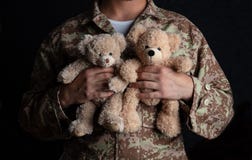 Νέος στρατιώτης που κρατά μια teddy αρκούδα στεμένος στο μαύρο υπόβαθρο στοκ εικόνα με δικαίωμα ελεύθερης χρήσης Νέος στρατιώτης που κρατά μια teddy αρκούδα στεμένος στο μαύρο υπόβαθρο στοκ εικόνα με δικαίωμα ελεύθερης χρήσης