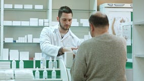Νέος φαρμακοποιός που δίνει το φάρμακο στον ανώτερο πελάτη ατόμων και που παίρνει την πληρωμή σε δολάρια στο φαρμακείο στοκ εικόνα με δικαίωμα ελεύθερης χρήσης Νέος φαρμακοποιός που δίνει το φάρμακο στον ανώτερο πελάτη ατόμων και που παίρνει την πληρωμή σε δολάρια στο φαρμακείο στοκ εικόνα με δικαίωμα ελεύθερης χρήσης