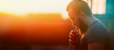 Νεαρός άνδρας με τα ζευγάρια σκλήρυνσης vaporiser στο υπόβαθρο ουρανού ηλιοβασιλέματος, θολωμένο υπόβαθρο, ιστοχώρος εμβλημάτων στοκ φωτογραφία Νεαρός άνδρας με τα ζευγάρια σκλήρυνσης vaporiser στο υπόβαθρο ουρανού ηλιοβασιλέματος, θολωμένο υπόβαθρο, ιστοχώρος εμβλημάτων στοκ φωτογραφία