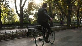 Νεαρός άνδρας με τα ακουστικά που οδηγούν το ποδήλατο στο πάρκο στο μαύρο ποδήλατο οδοιπορίας Οδήγηση με τα nohands ακούοντας φιλμ μικρού μήκους Νεαρός άνδρας με τα ακουστικά που οδηγούν το ποδήλατο στο πάρκο στο μαύρο ποδήλατο οδοιπορίας Οδήγηση με τα nohands ακούοντας φιλμ μικρού μήκους