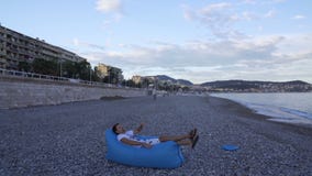 Νεαρός άνδρας που διογκώνει και που ξαπλώνει στον καναπέ πολυσύχναστων μερών για να απολαύσει το υπόλοιπο στην παραλία θάλασσας απόθεμα βίντεο Νεαρός άνδρας που διογκώνει και που ξαπλώνει στον καναπέ πολυσύχναστων μερών για να απολαύσει το υπόλοιπο στην παραλία θάλασσας απόθεμα βίντεο