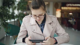 Ο έφηβος κοριτσιών στα γυαλιά χρησιμοποιεί ένα smartphone σε έναν πίνακα σε φιλμ μικρού μήκους Ο έφηβος κοριτσιών στα γυαλιά χρησιμοποιεί ένα smartphone σε έναν πίνακα σε φιλμ μικρού μήκους