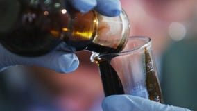Ο βοηθός χύνει το ακατέργαστο πετρέλαιο από το βολβό στο ποτήρι εργαστηρίων Ο βοηθός χύνει το ακατέργαστο πετρέλαιο από το βολβό στο ποτήρι εργαστηρίων
