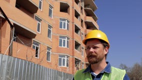 Ο διευθυντής κατασκευής σε ένα κίτρινο κράνος με μια γενειάδα και mustache μιλά ενάντια στο εργοτάξιο οικοδομής 4 Κ φιλμ μικρού μήκους Ο διευθυντής κατασκευής σε ένα κίτρινο κράνος με μια γενειάδα και mustache μιλά ενάντια στο εργοτάξιο οικοδομής 4 Κ φιλμ μικρού μήκους